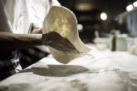 Pizzaiolo che stende un impasto per pizza in teglia