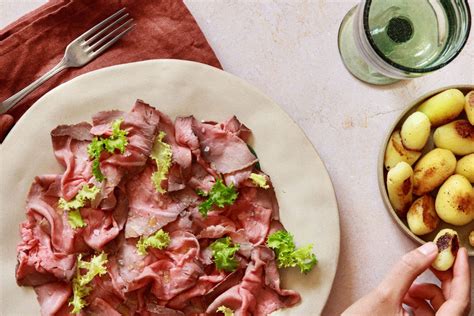 Un piatto di roast beef affettato sottilmente con contorno di patate