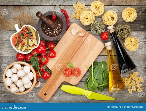 Ingredienti freschi per la pasta e per il pesto di olive su un tavolo di legno.