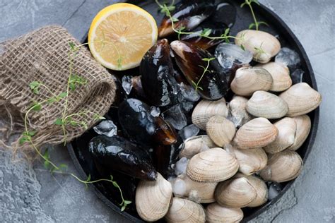 Un primo piano di gamberi, cozze, vongole e cubetti di pesce spada in una padella, con pomodorini e aromi.